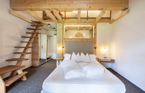 A bedroom with a large bed, wooden staircase, and a view of a balcony. - Berghotel Jochgrimm - Your hoome in the Dolomites (Aldino)