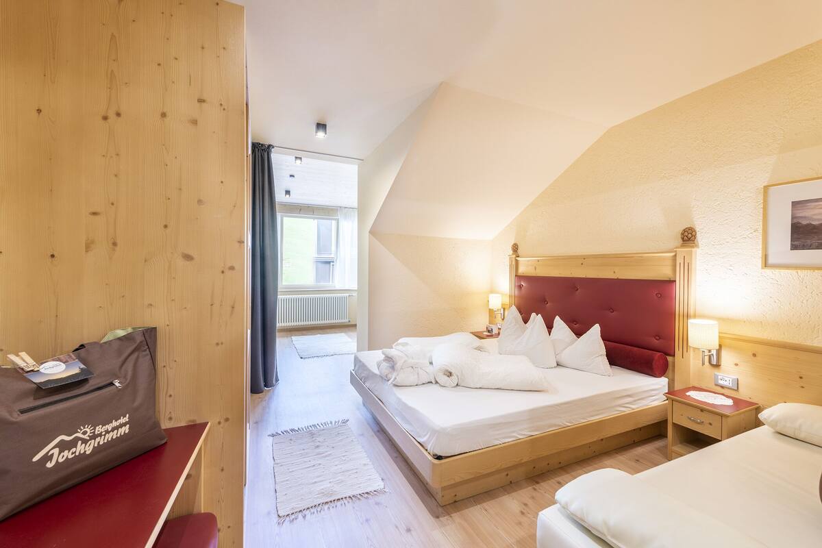 A hotel room with a wooden headboard, a bed with white linens, a bedside table, and a view of a balcony.