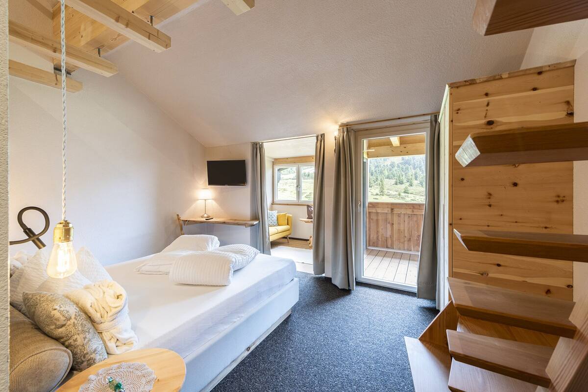 A bedroom with a bed, bedside table, lamp, and a view of the outdoors.