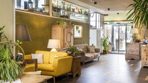 Een ruime lobby met een gele bank, houten kasten en potplanten.