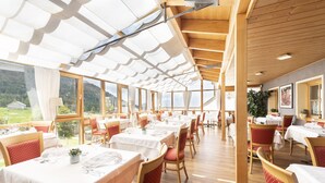 Een restaurant met meerdere tafels en stoelen, grote ramen en een houten plafond.