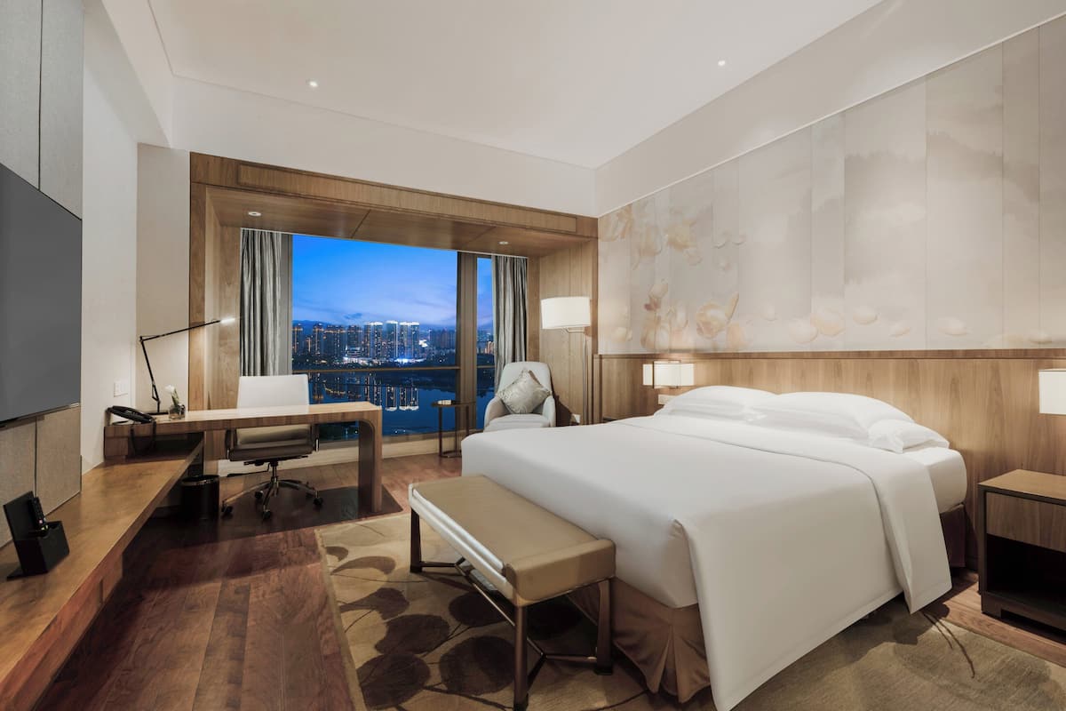 Ett hotellrum med en stor säng, ett skrivbord, en stol och utsikt över stadsbilden.
