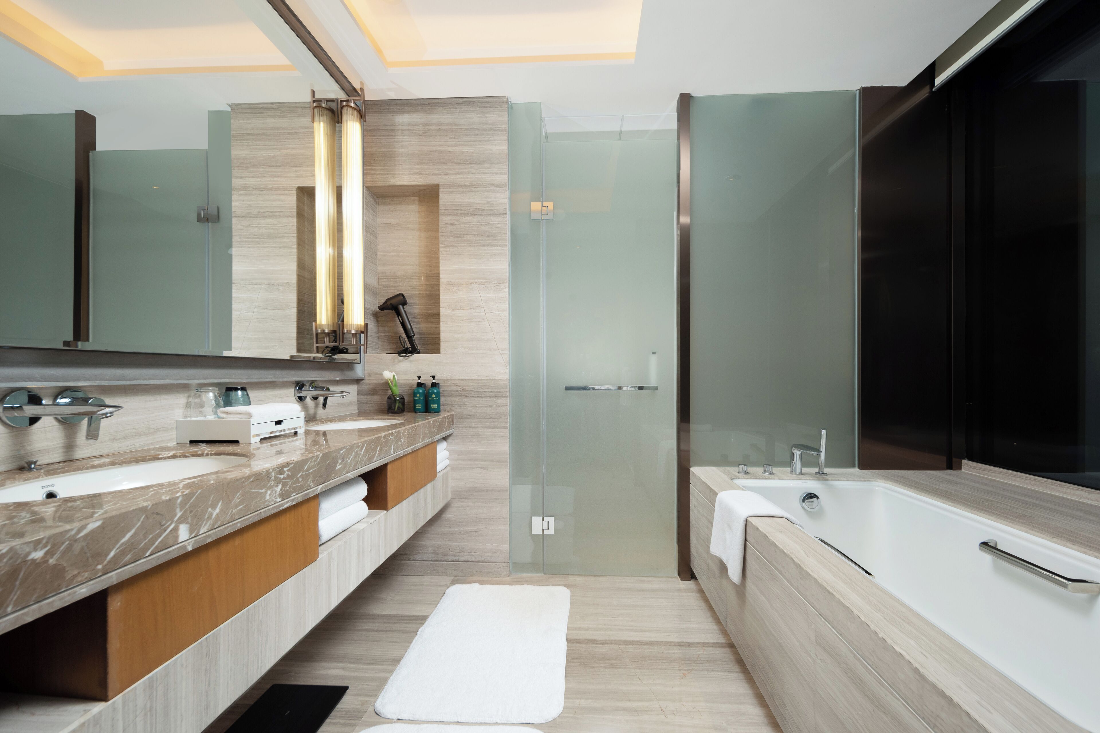 A modern bathroom with a large mirror, two sinks, a bathtub, and a glass shower enclosure.