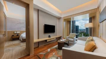 A modern hotel room with a large TV, a sofa, a coffee table, and a city view.