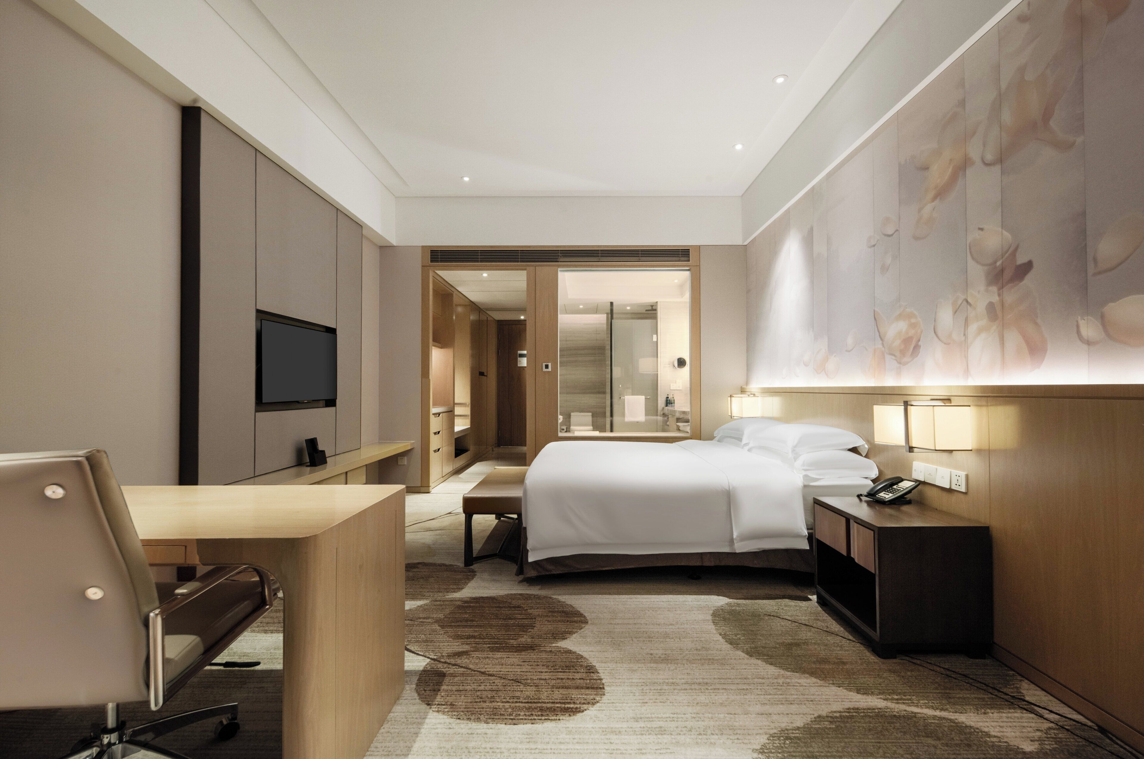 Une chambre d’hôtel moderne équipée d’un lit, d’un bureau, d’une chaise, d’une table de chevet et d’un téléviseur.