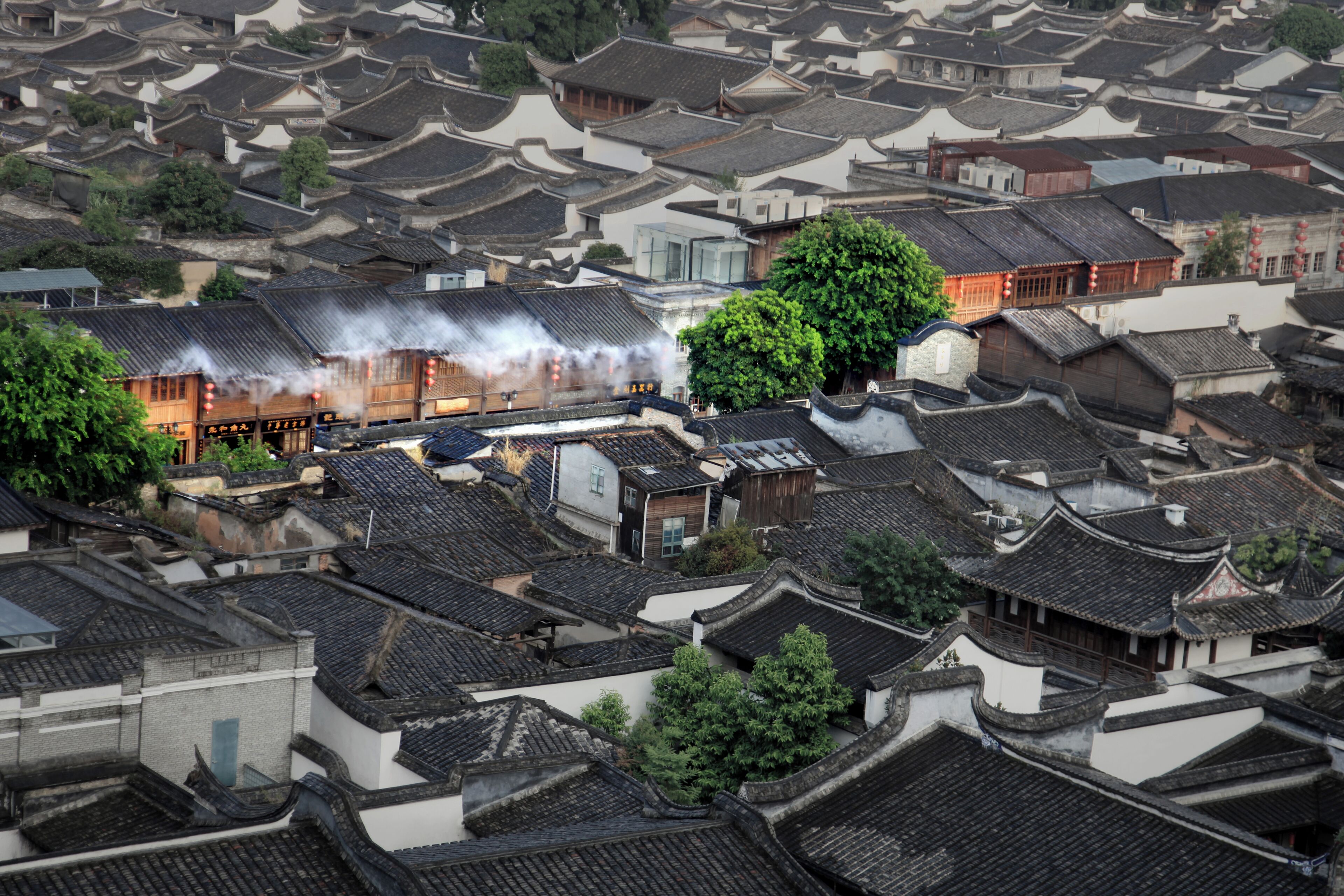 A traditional Chinese courtyard with tiled roofs and wooden buildings, surrounded by greenery.