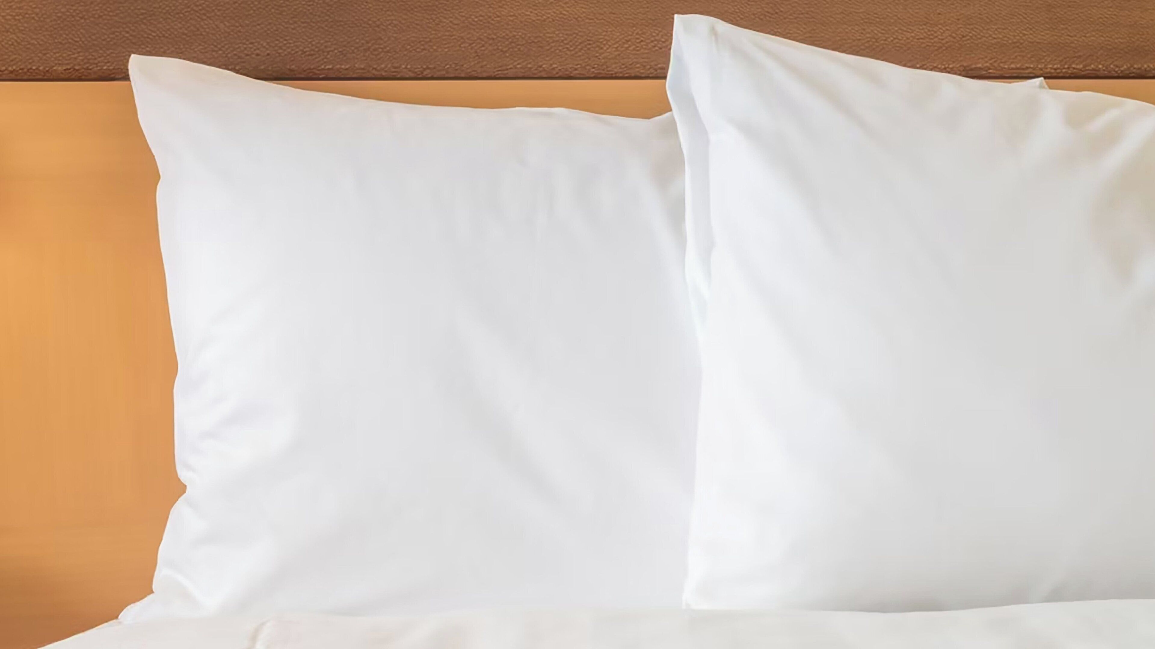 Ein Bett mit weißer Bettwäsche und Kissen vor einem Holz-Kopfteil.