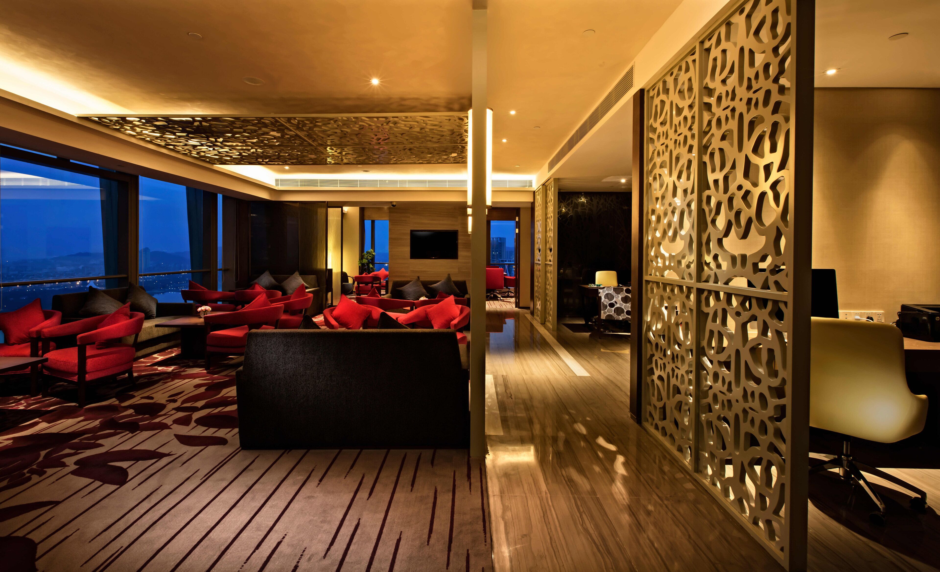A modern hotel lobby with a large seating area, a TV, and a decorative partition.