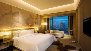 A hotel room with a large bed, a sofa, a TV, and a city view.