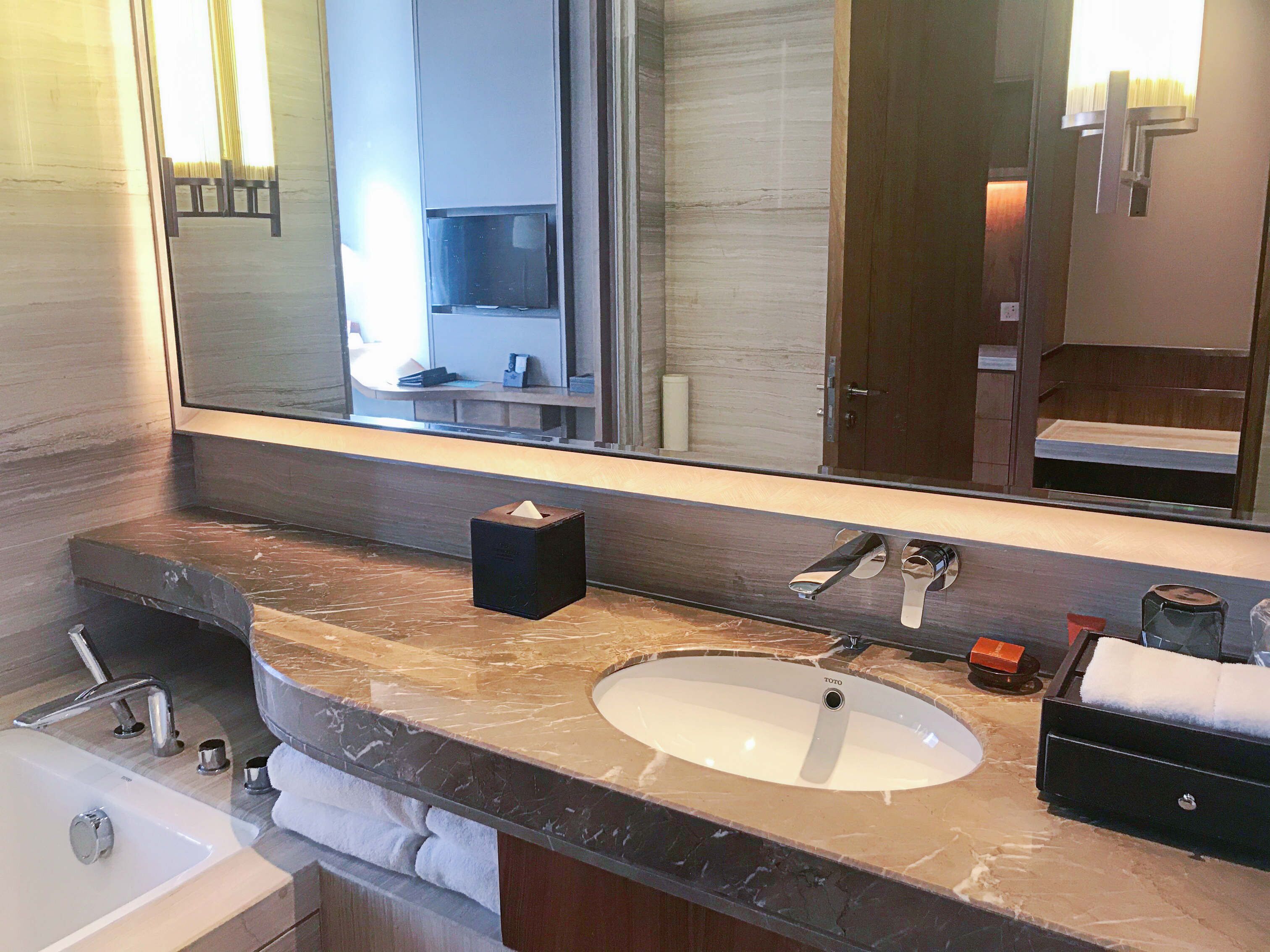 Ein modernes Badezimmer mit großem Spiegel, Waschbecken, Badewanne und einem Waschtisch mit Handtuchhalter.