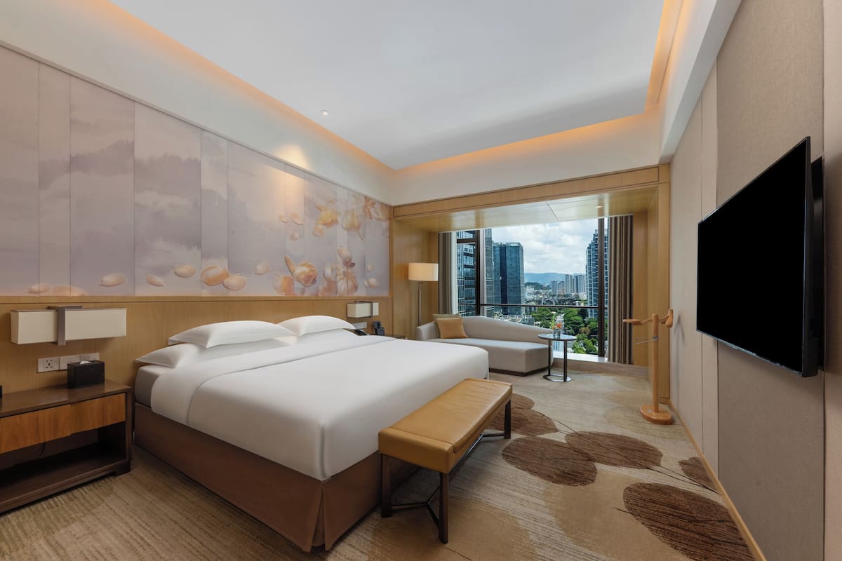 Ett modernt hotellrum med en stor säng, en soffa, en TV och utsikt över staden.