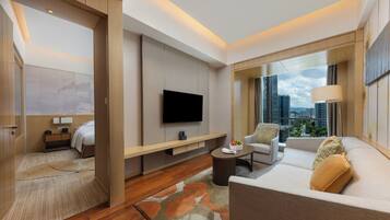 A modern hotel room with a flat-screen TV, a sofa, a coffee table, and a city view through large windows.