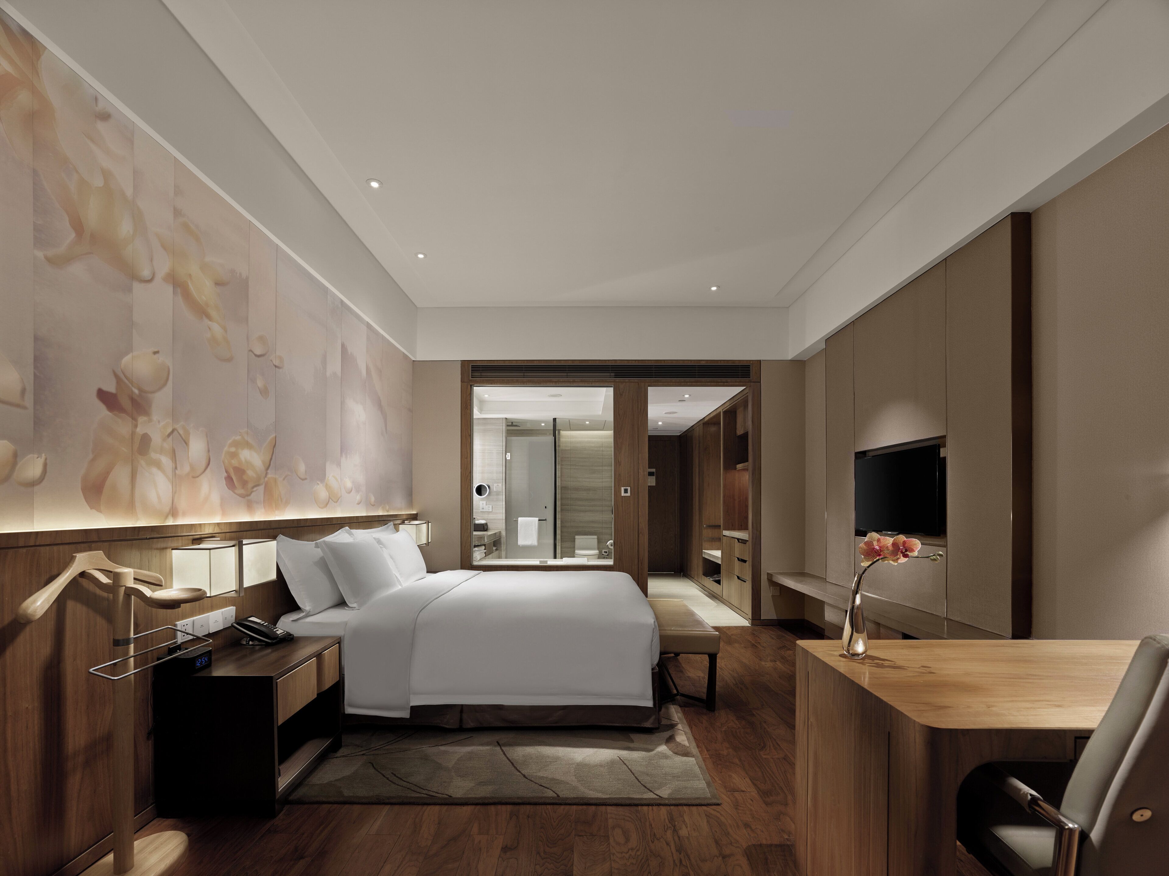 Une chambre d’hôtel moderne, dotée d’un grand lit, d’un bureau, d’une télévision et d’une salle de bain visible à travers une porte ouverte.