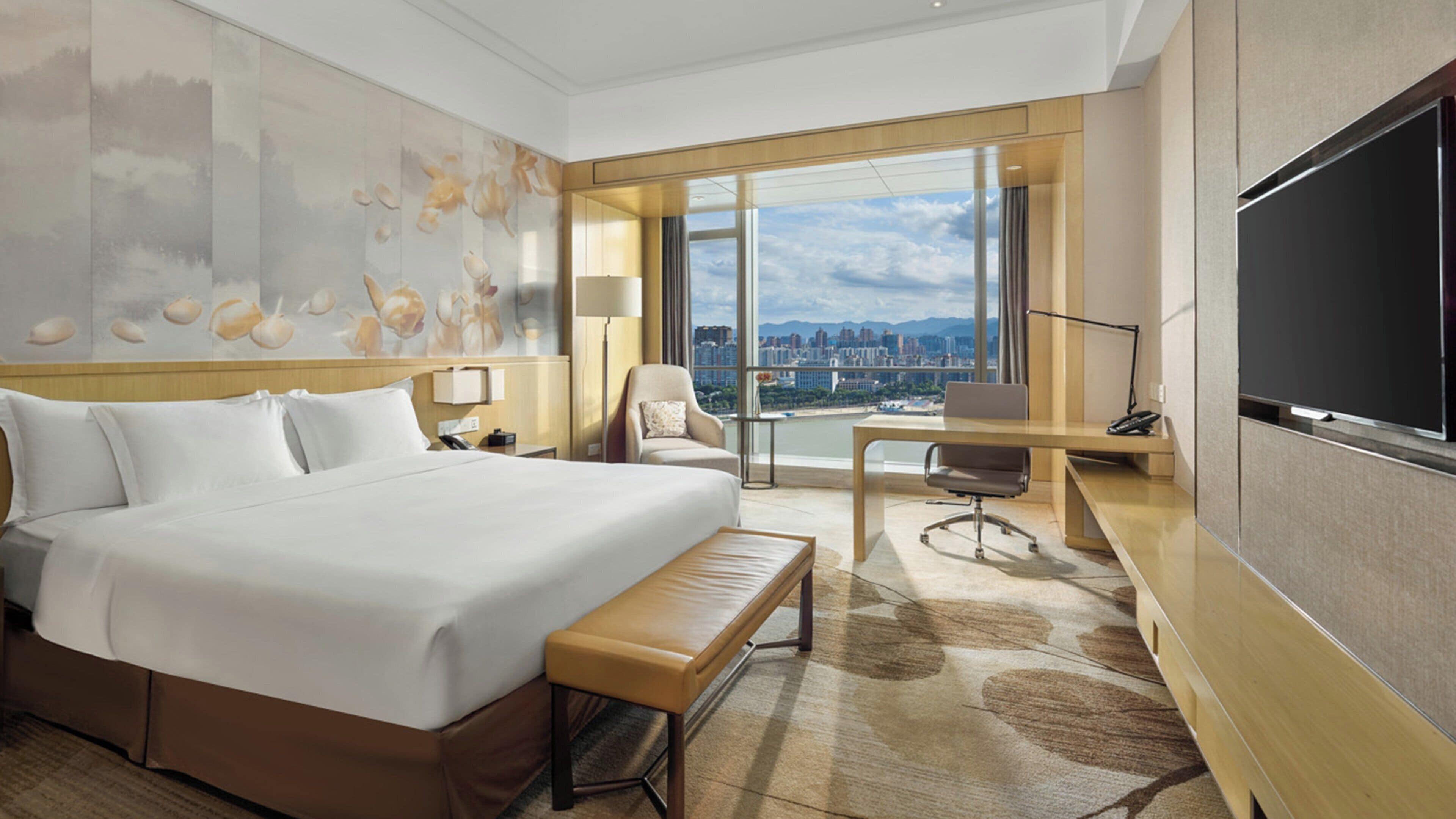A hotel room with a large bed, a desk, a chair, and a TV.