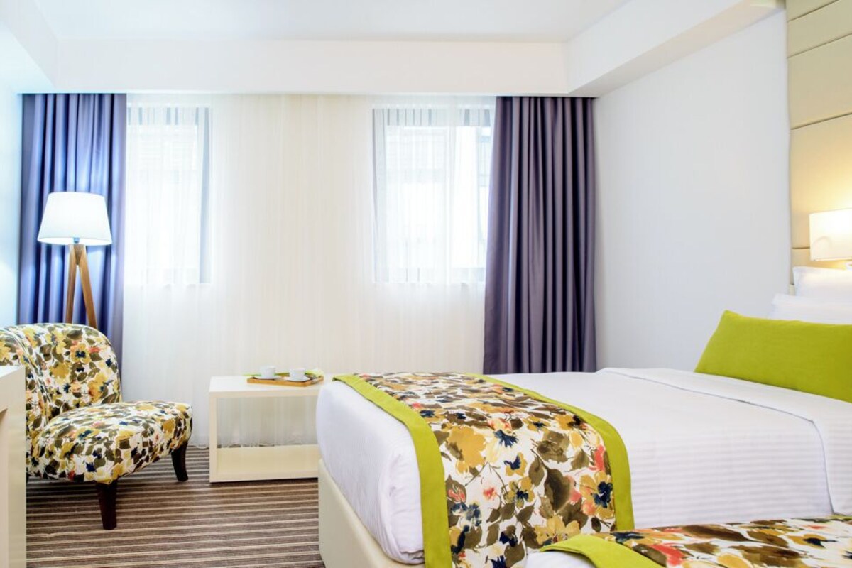 A hotel room with a bed, a chair, a desk, a lamp, and a mirror.