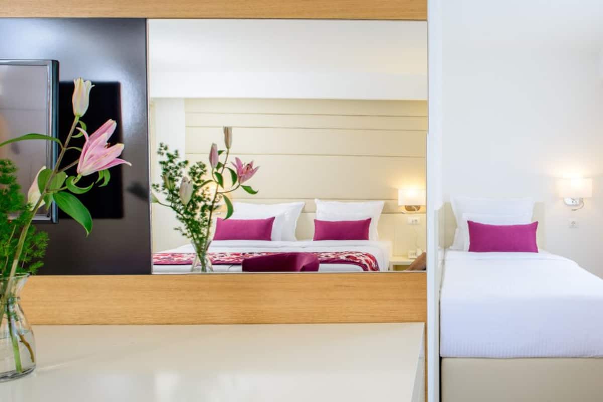 A hotel room with a bed, a nightstand, a mirror, and a vase with flowers.