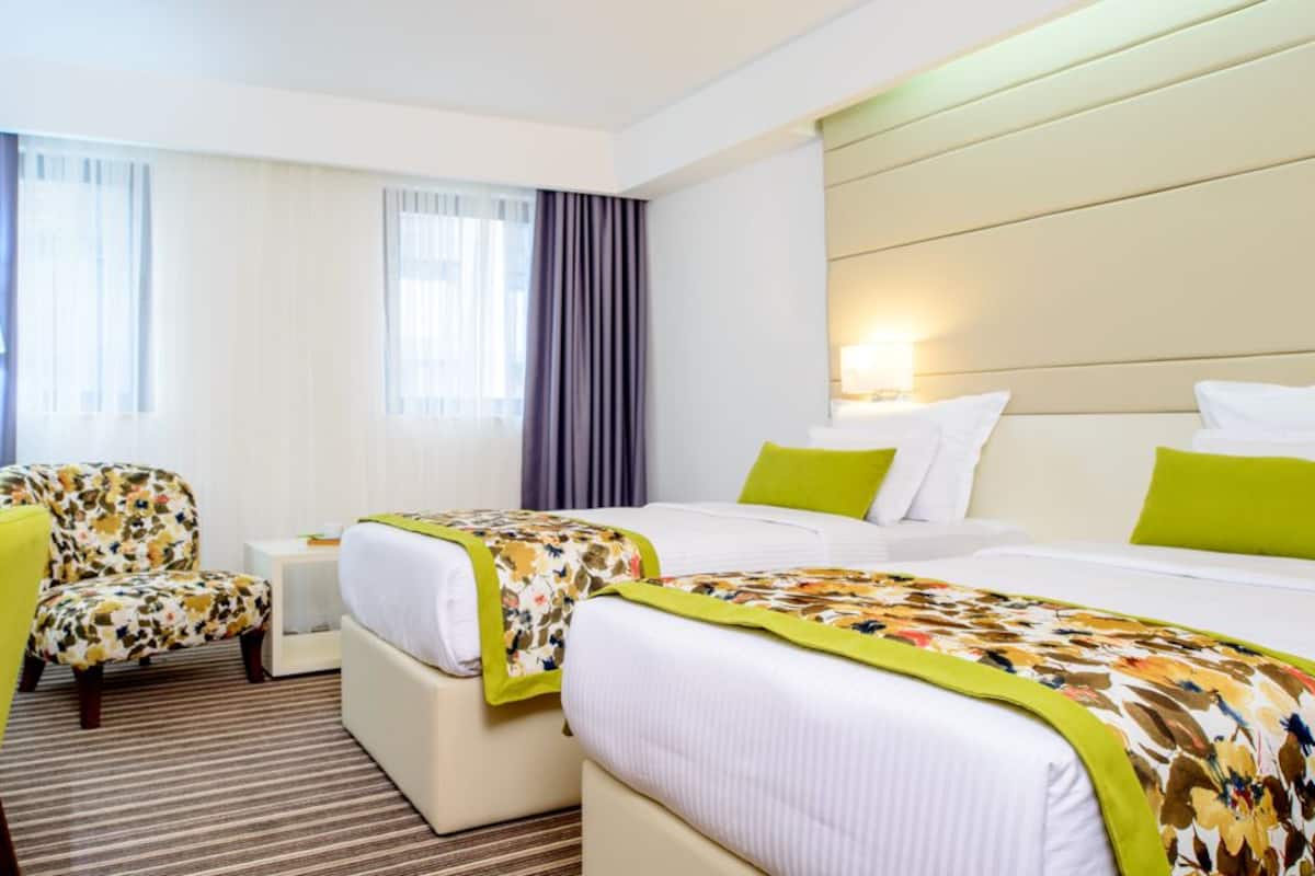 A hotel room with a desk, two beds, a chair, and a vase of flowers.