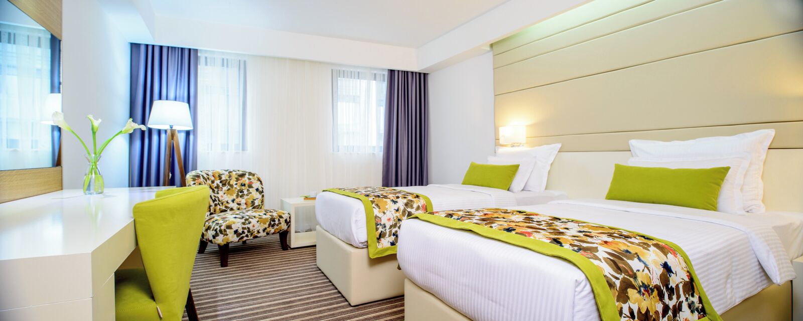 Ein Hotelzimmer mit Schreibtisch, zwei Betten, einem Sessel und einem Blumenstrauß.