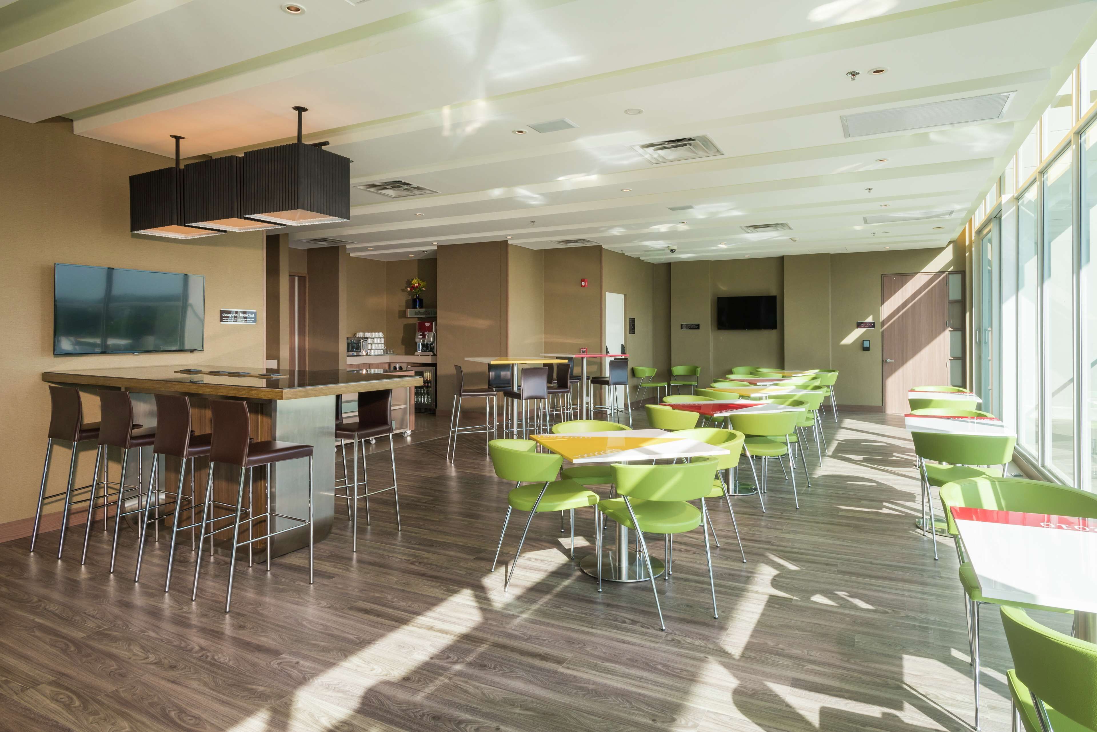 A modern dining area with green chairs and tables, a bar area, and a flat-screen TV mounted on the wall.