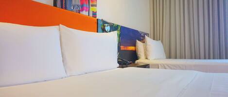 Habitación de hotel con dos camas, ropa de cama blanca, un tapiz colorido y un ventanal con cortinas.