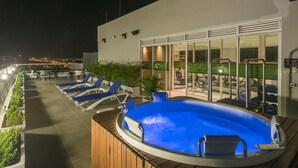 Un área de piscina en la azotea con sillones de descanso y un jacuzzi.
