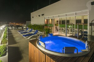Un área de piscina en la azotea con sillones de descanso y un jacuzzi.