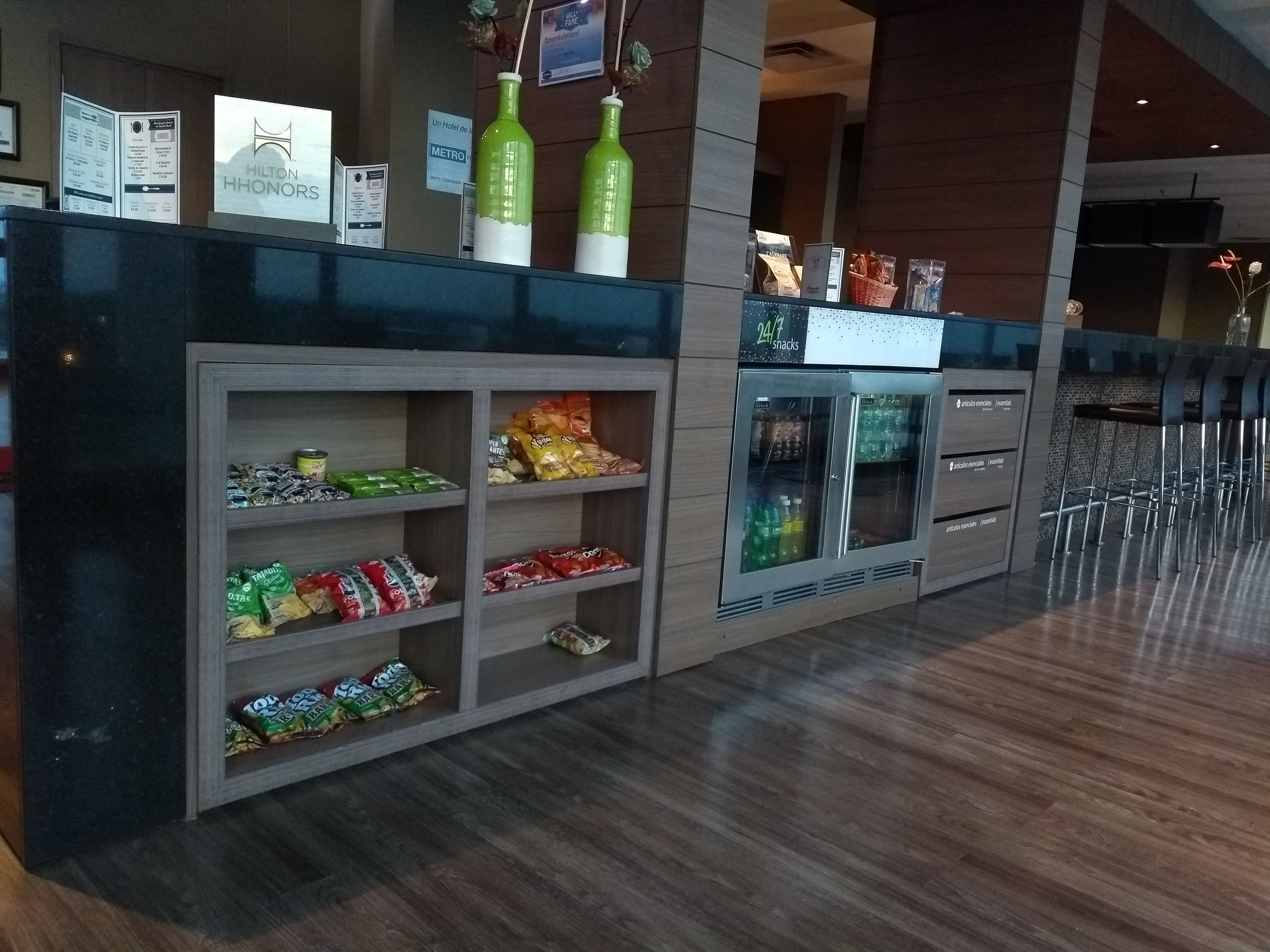 A hotel reception area with snack dispensers, a 24/7 snack machine, and a seating area with metal chairs.