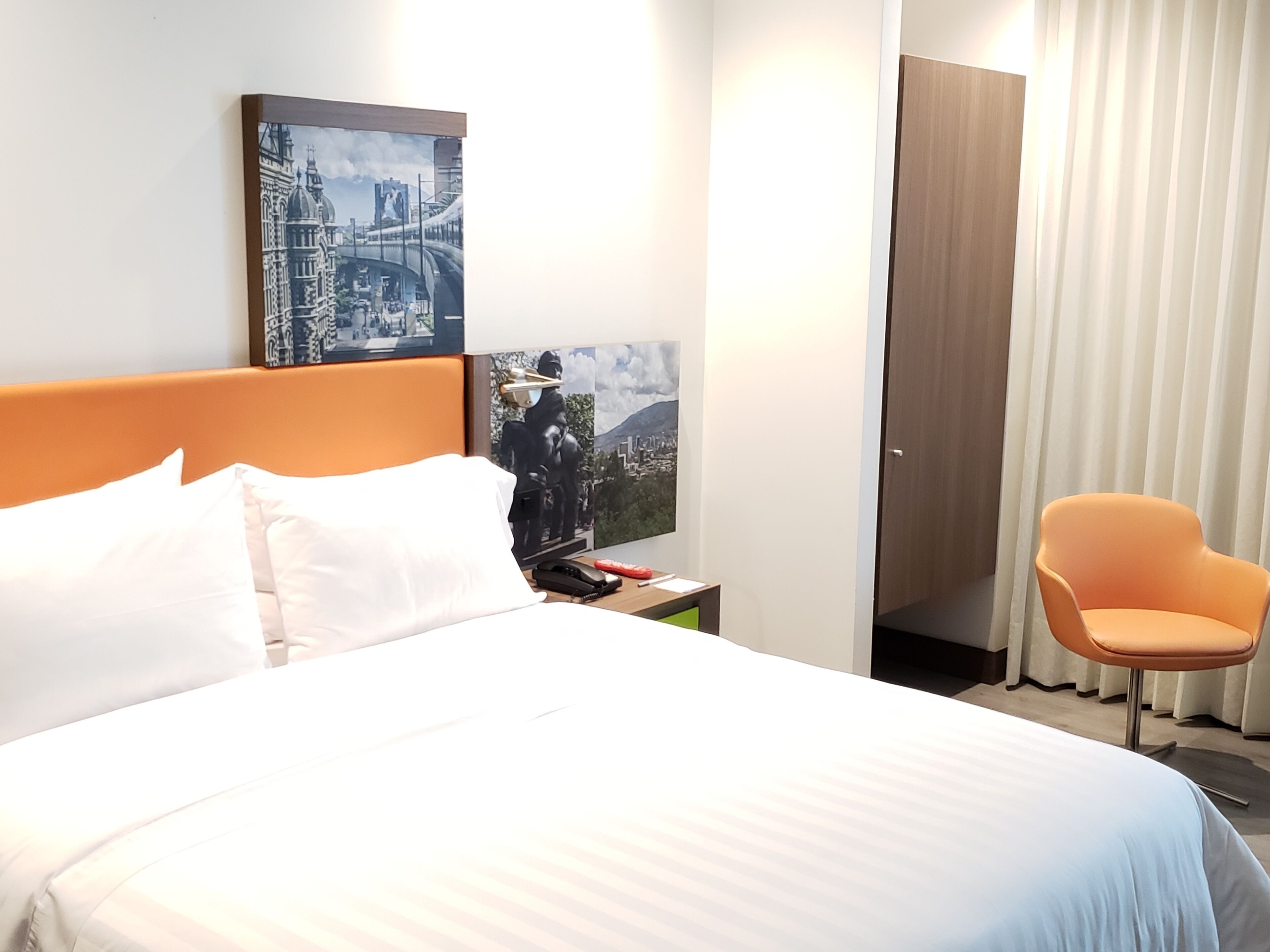 Une chambre d’hôtel avec un grand lit, une table de chevet, une chaise et deux œuvres d’art murales.
