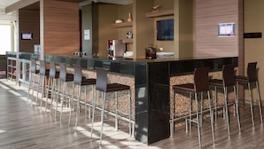 Un área de bar moderna con una barra larga, varios taburetes y una pantalla de televisión.