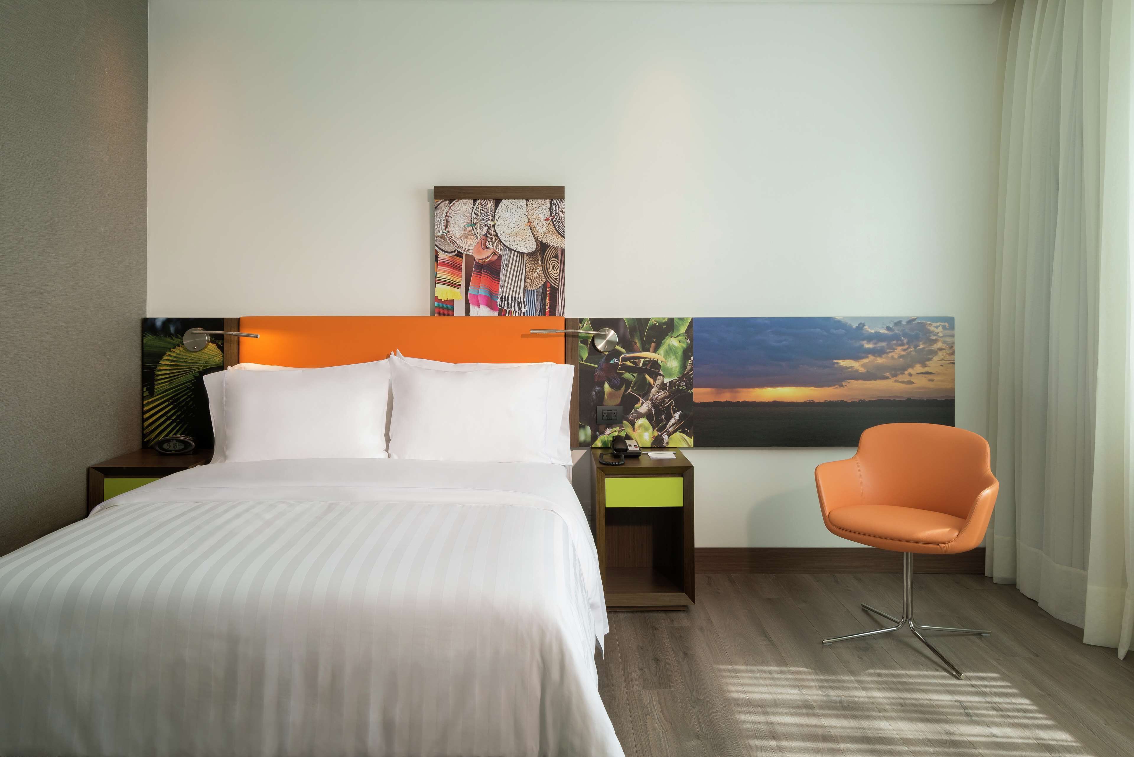 A hotel room with a bed, a nightstand, a chair, and a large painting on the wall.