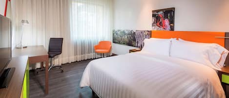Habitación de hotel con una cama grande, un escritorio con silla, una mesita y una ventana con cortinas.