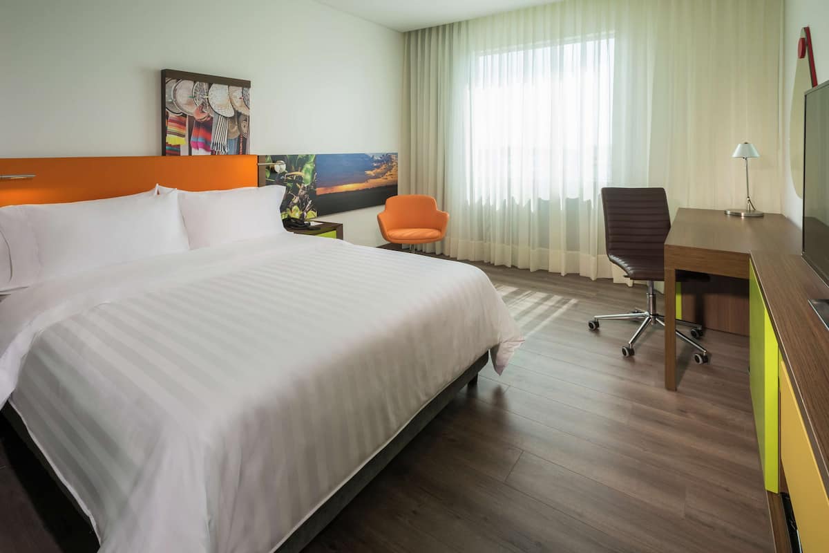 Una habitación de hotel con una cama grande, un escritorio, una silla naranja y un cuadro en la pared.