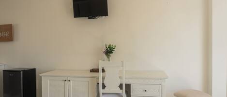 A room with a white desk, a chair, a small cabinet, a television, and an air conditioner.