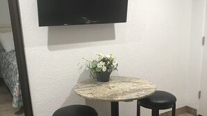 A small room with a round table, two stools, a potted plant, a flat-screen TV, and a bed with a floral bedspread. - Pyramid Resort Motel (Wildwood Crest)