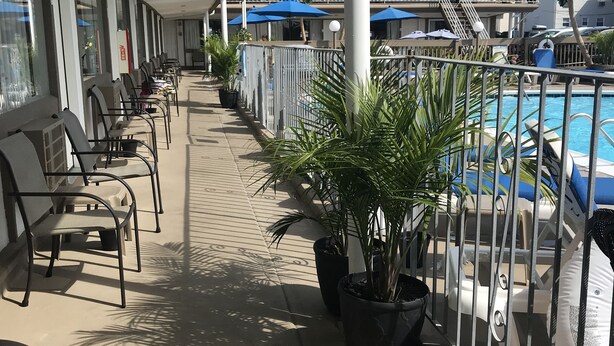 A balcony with chairs and potted plants, overlooking a pool area with umbrellas and lounge chairs. - Pyramid Resort Motel (Wildwood Crest)
