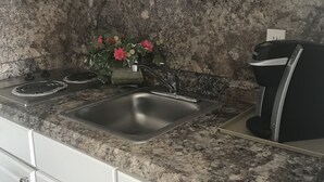 A kitchen with white cabinets, a granite countertop, a stainless steel sink, a coffee maker, and a vase with flowers. - Pyramid Resort Motel (Wildwood Crest)