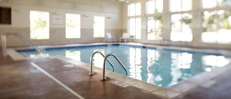 An indoor swimming pool with clear water, a diving board, and a tiled floor.