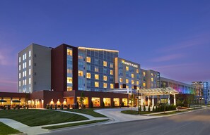 A multi-story hotel with a modern design, featuring a prominent entrance with a glass canopy and a well-lit facade. - Hyatt Place Lansing - East (Lansing)