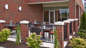 A brick building with outdoor seating, a glass door entrance, and a metal fence.
