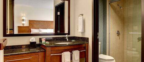 A hotel bathroom with a wooden vanity, a large mirror, a sink, a toilet, and a glass-enclosed shower.
