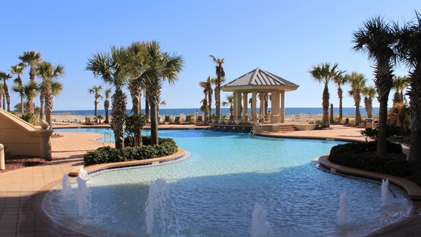 A resort pool with palm trees, a gazebo, and a view of the ocean. - Indigo by Luxury Coastal Vacations (Pensacola)