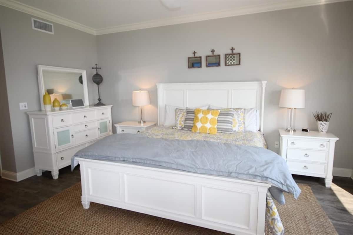 A bedroom with a large bed, two nightstands, a dresser, and a mirror.