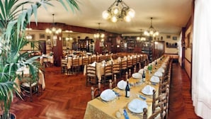 Een ruime eetzaal met houten vloeren, meerdere gedekte tafels en hangende kroonluchters.