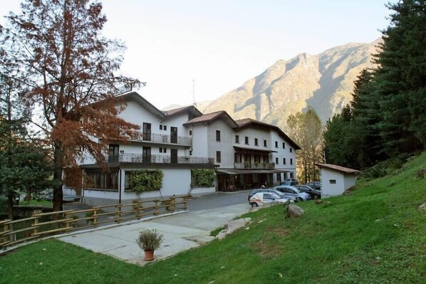 A multi-story hotel with a balcony, parking area, and a mountainous backdrop. - Albergo Il Castellino (Darfo Boario Terme)