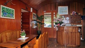 Een houten interieur met een receptiebalie, houten banken en een plant in pot.