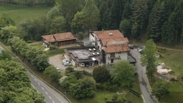 Vista aérea de un hotel con un edificio central y dos estructuras más pequeñas, rodeado de vegetación y una carretera.