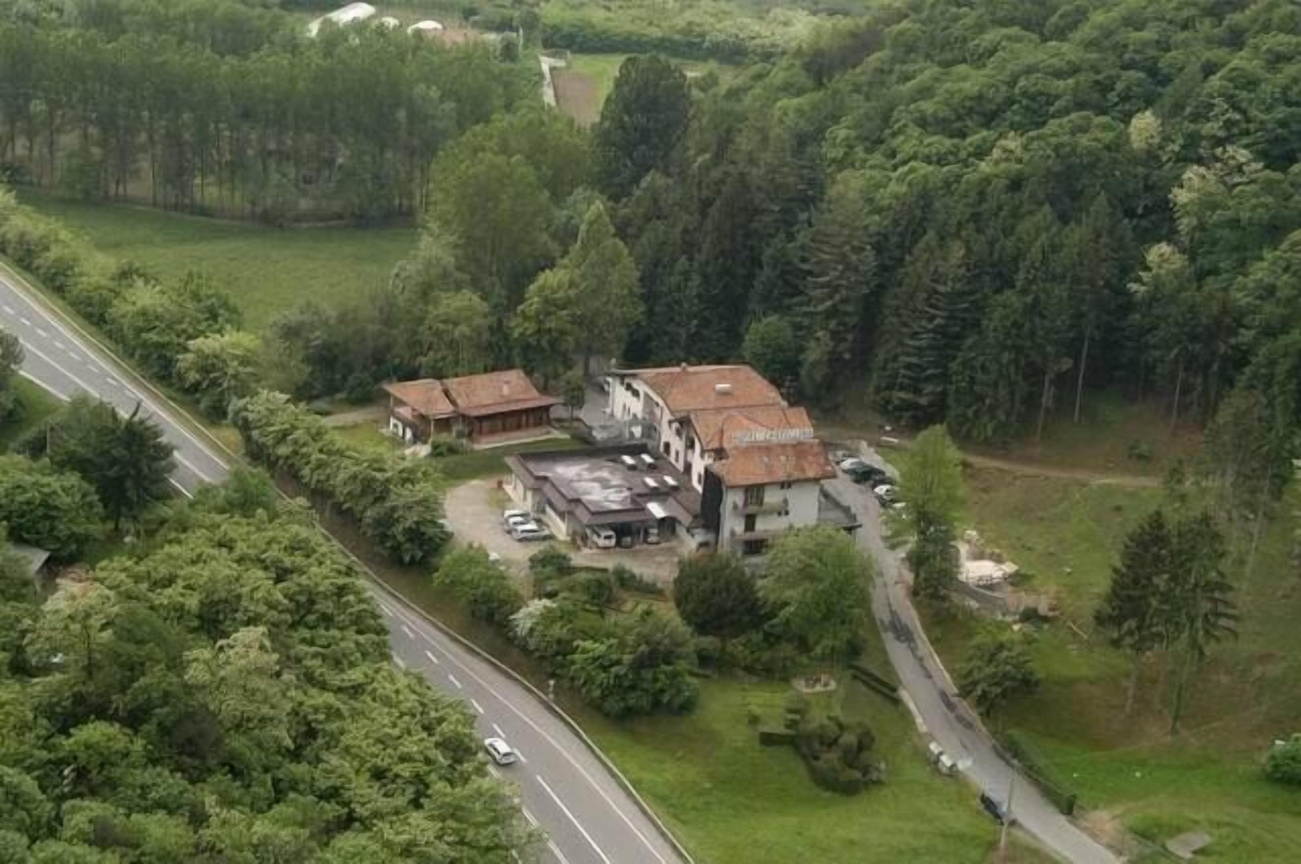 Vista aérea de una propiedad con un edificio principal y dos construcciones más pequeñas, rodeada de un bosque denso.