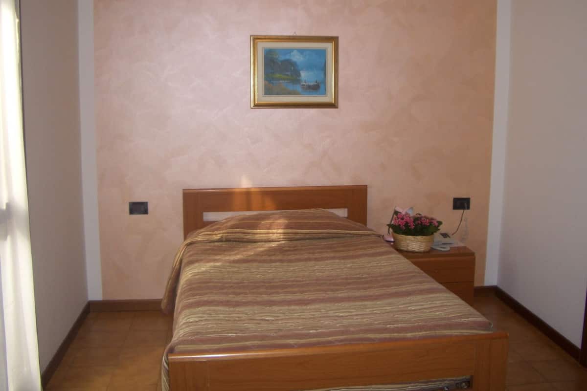 A bedroom with a wooden bed, a framed picture on the wall, and a nightstand with a basket of flowers.