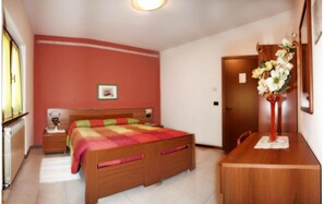 A bedroom with a wooden bed, a nightstand, a desk, and a vase of flowers. - Albergo Il Castellino (Darfo Boario Terme)