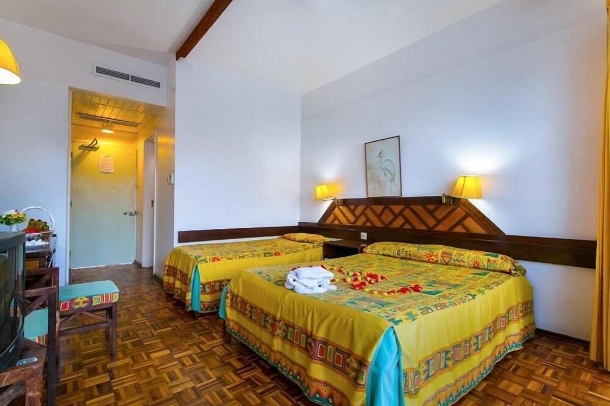A hotel room with two beds, wooden flooring, a television, and a desk with a chair.